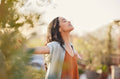 Woman standing outdoors with arms outstretched, her face turned upward as she smiles. She is surrounded by nature.