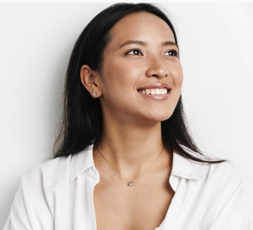 Woman smiling as she looks up and to the left, wearing a white shirt and a necklace with a clear background.